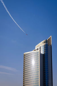 Low angle view of a skyscraper against blue sky and an airplane doing an airshow in abu dhabi uae. 