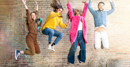 Full length of friends jumping against wall