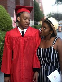 Woman looking at friend wearing graduation gown on road