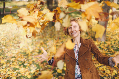 Young woman playing with autumn leaves at park