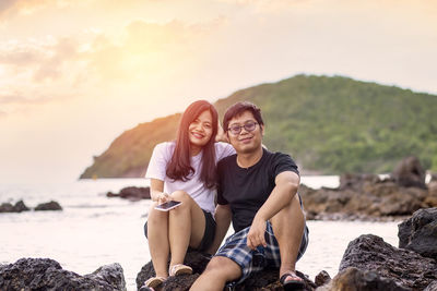 Young woman sitting on rock by sea against sky