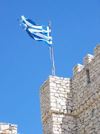 Low angle view of greek flag waving on fort against clear blue sky
