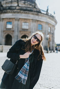 Portrait of young woman standing against building