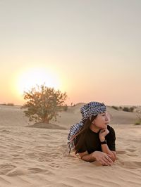 Full length of girl sitting on sand at beach against sky during sunset
