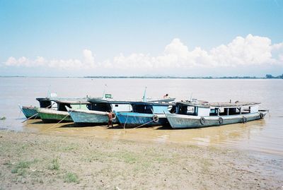 Boats moored at beach against sky on sunny day