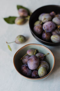 Close up of bowls of fresh plums against a marble background.