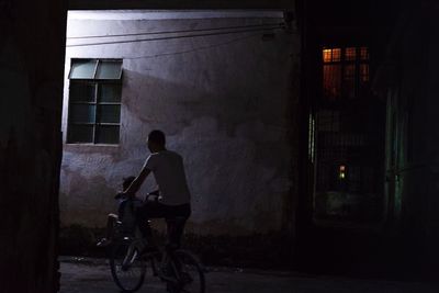 Rear view of man riding bicycle on street against building at night
