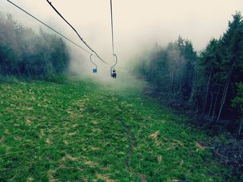 Ski lifts over grassy field during foggy weather