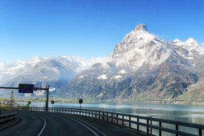 Road by snowcapped mountains against clear sky