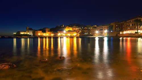 Illuminated cityscape by sea against sky at night