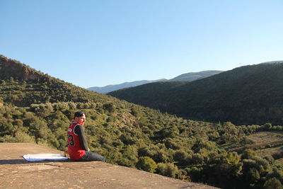 Man sitting on mountain against sky