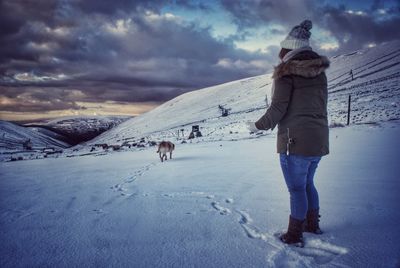 Woman standing on snowy field against cloudy sky during sunset