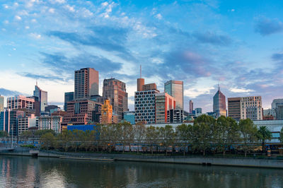 Modern buildings by river against sky in city