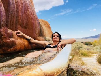 Mid adult woman in bathtub by rocks against sky
