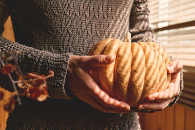 Female in knitted brown woolen sweater holding orange pumpkin. cozy autumn vibes. fall mood.