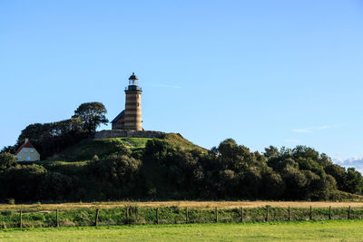 Lighthouse by trees on field against sky