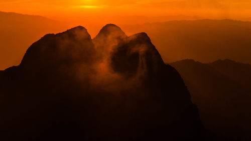 Scenic view of silhouette mountains against orange sky