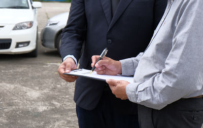 Midsection of client signing document while businessman holding clipboard at street