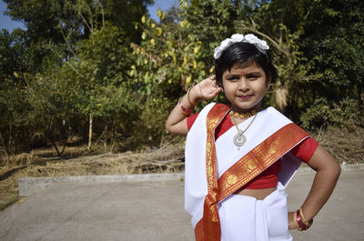 Cute smiling girl wearing white sari while standing in park during sunny day