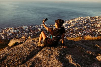 Side view of woman sitting on rock at beach