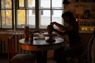 Pottery studio interior. woman ceramics master shaping potter vase with special tools for raw clay