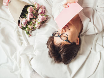 High angle view of smiling woman holding envelope lying on bed at home