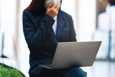 Midsection of businesswoman using laptop while sitting outdoors