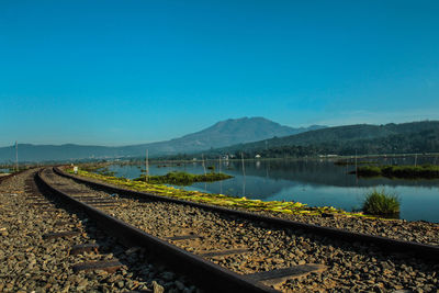 Railroad tracks by lake against clear blue sky