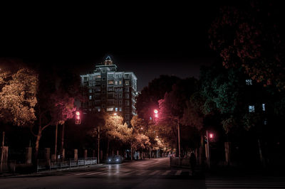 Illuminated street amidst buildings against sky at night