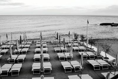 Deck chairs with parasols at beach against sky