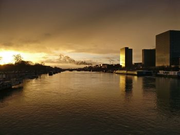 Scenic view of river by buildings against sky at sunset