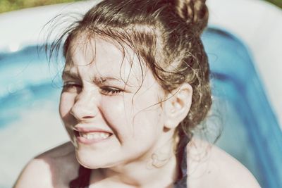 Close-up of cheerful wet girl against swimming pool during sunny day