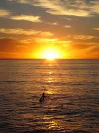 Silhouette surfers in sea against orange sky