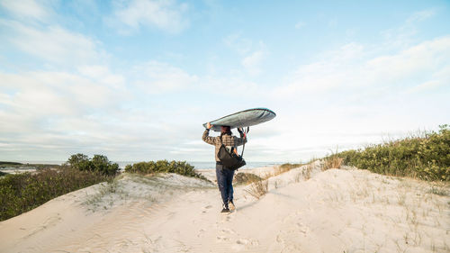 Full length of man with surfboard walking at beach against sky