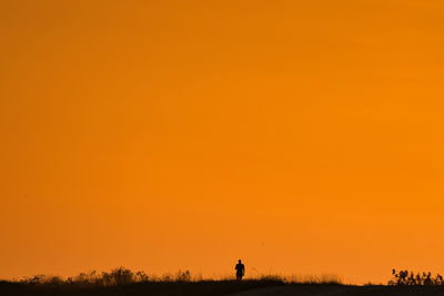 Silhouette people on field against orange sky