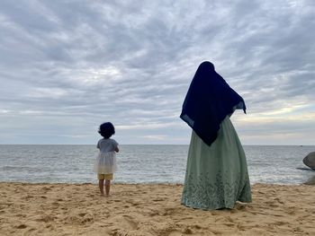 Rear view of women standing at beach against sky