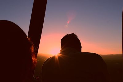 Rear view of silhouette friends in hot air balloon during sunset