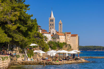 Buildings by sea against clear blue sky