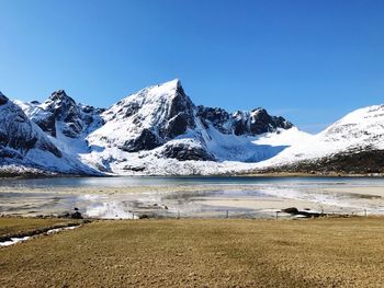 Scenic view of snowcapped mountains by sea against clear blue sky