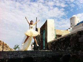 Full length of happy bride jumping on street against sky