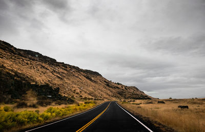 Empty road by mountain against cloudy sky