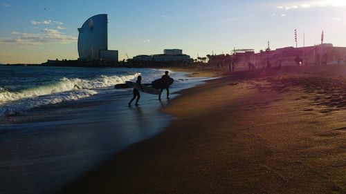 Silhouette people riding on beach in city against sky