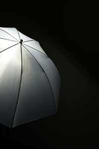 Low angle view of electric light emitting behind umbrella against black background