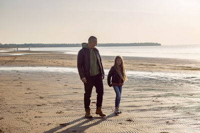 Father walks with  daughter near the sea sandy beach in afternoon in autumn in leather jackets