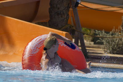 Caucasian blonde woman descended from the water slide on the circle and laughs, in the pool 