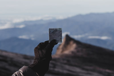Cropped hand of person holding paper currency on mountains against sky