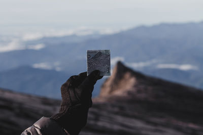 Person hand holding stick in mountains against sky