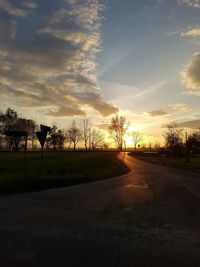 Road by silhouette trees against sky during sunset