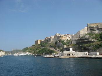 Buildings by sea against clear blue sky