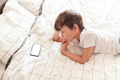 Child sitting relaxed in bed cross-legged and playing on smartphone